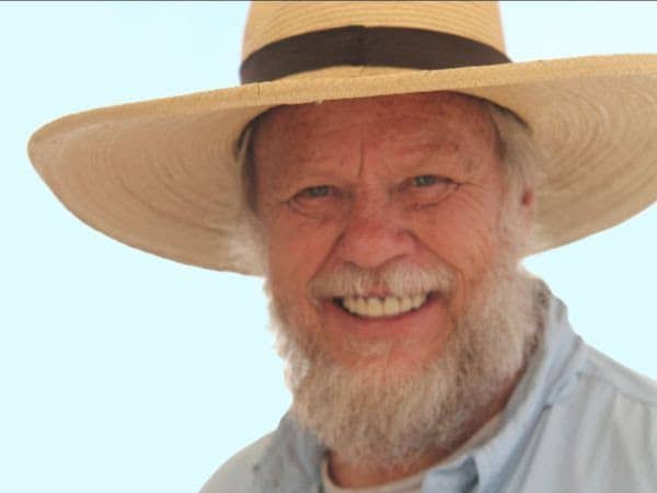 A color photograph of Hermann Trappman smiling. He is wearing a hat and a collared shirt.